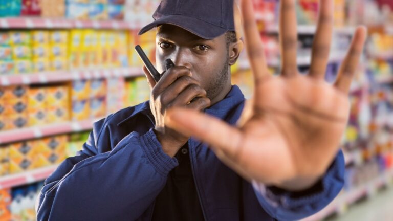 Digital composite of security guard of the supermarket saying stop with his hand (blurred) and speaking with the walkie-t.