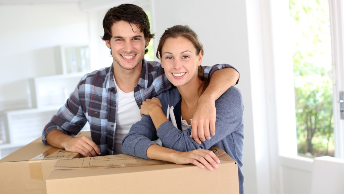 Smiling couple leaning on boxes in new home.
