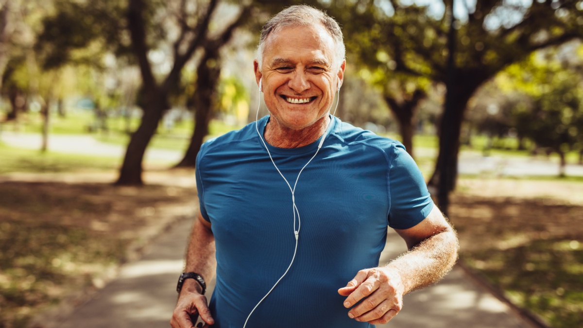 Portrait of a senior man in fitness wear running in a park. Close up of a smiling man running while listening to music using earphones.