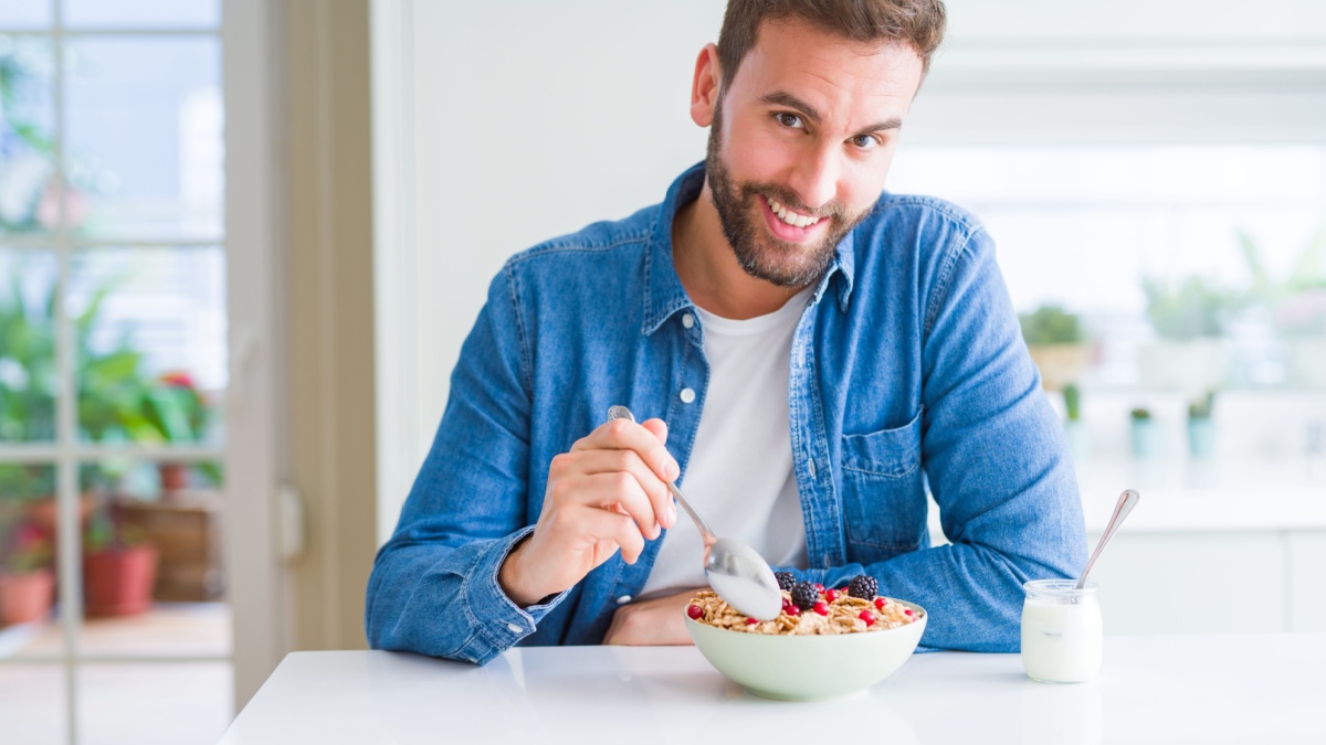 Handsome man having breakfast eating cereals at home and smiling.