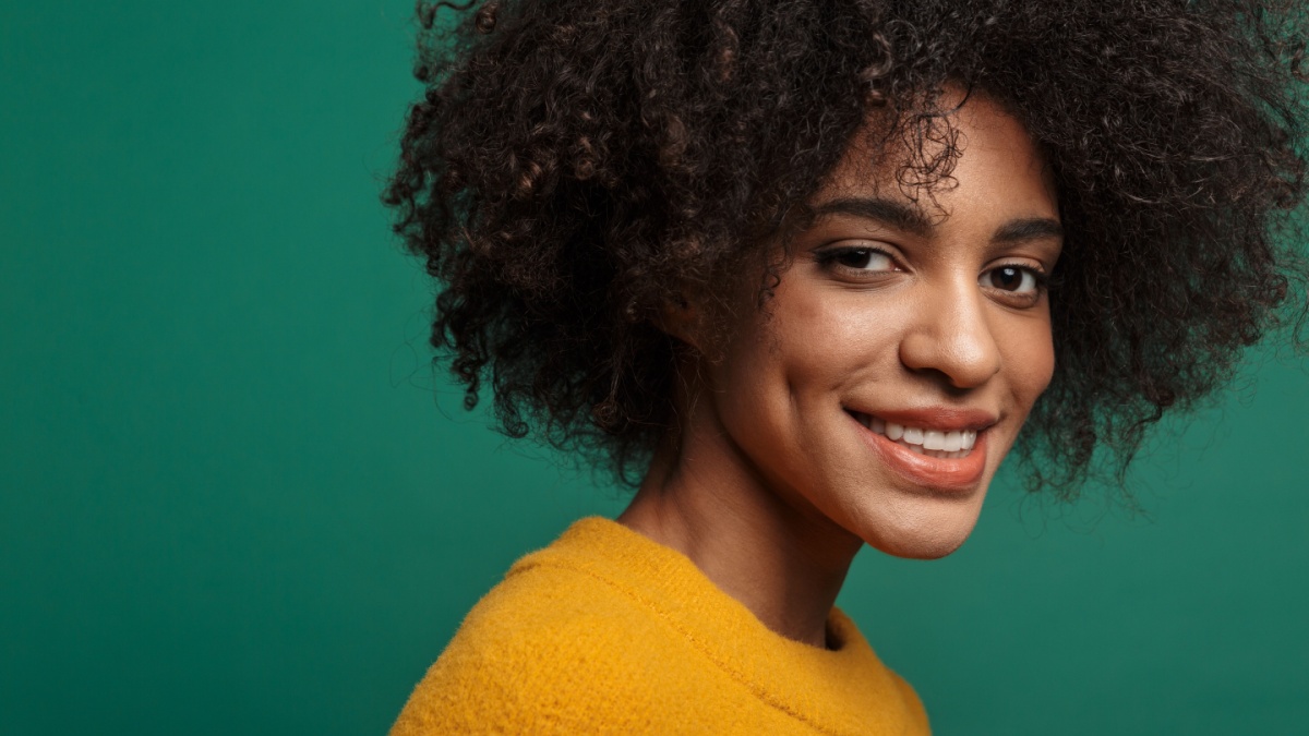 Image of a beautiful happy cheery pleased african curly woman posing isolated over dark blue wall background.
