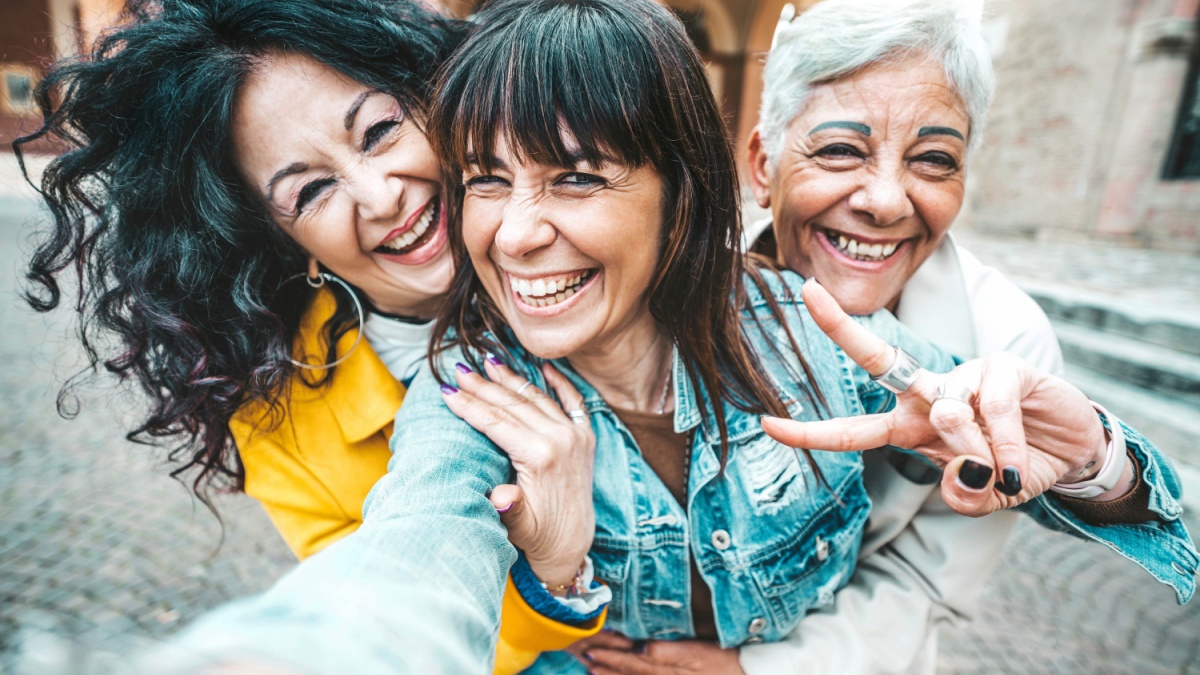 Three senior women taking selfie photo with smart mobile phone device outside.