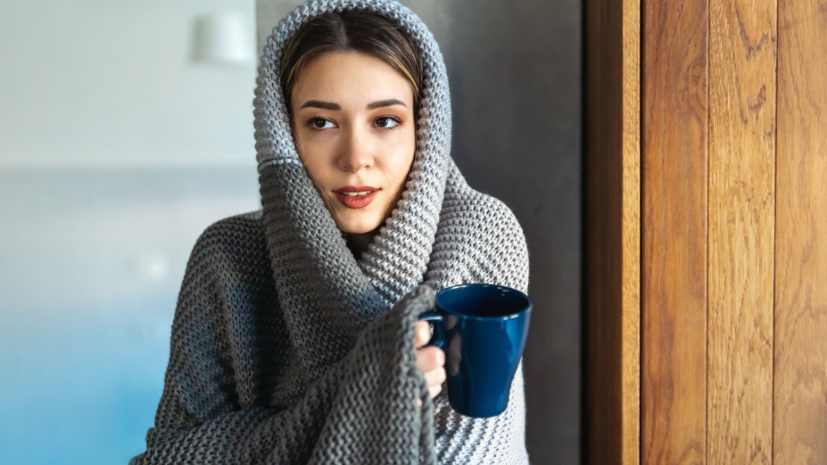 Freezing woman covered with a cozy blanket. Female wrapped in warm blanket, drinking hot drink.