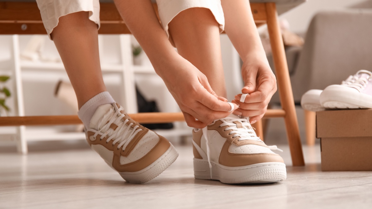 Woman in stylish sneakers tying shoe lace, closeup.