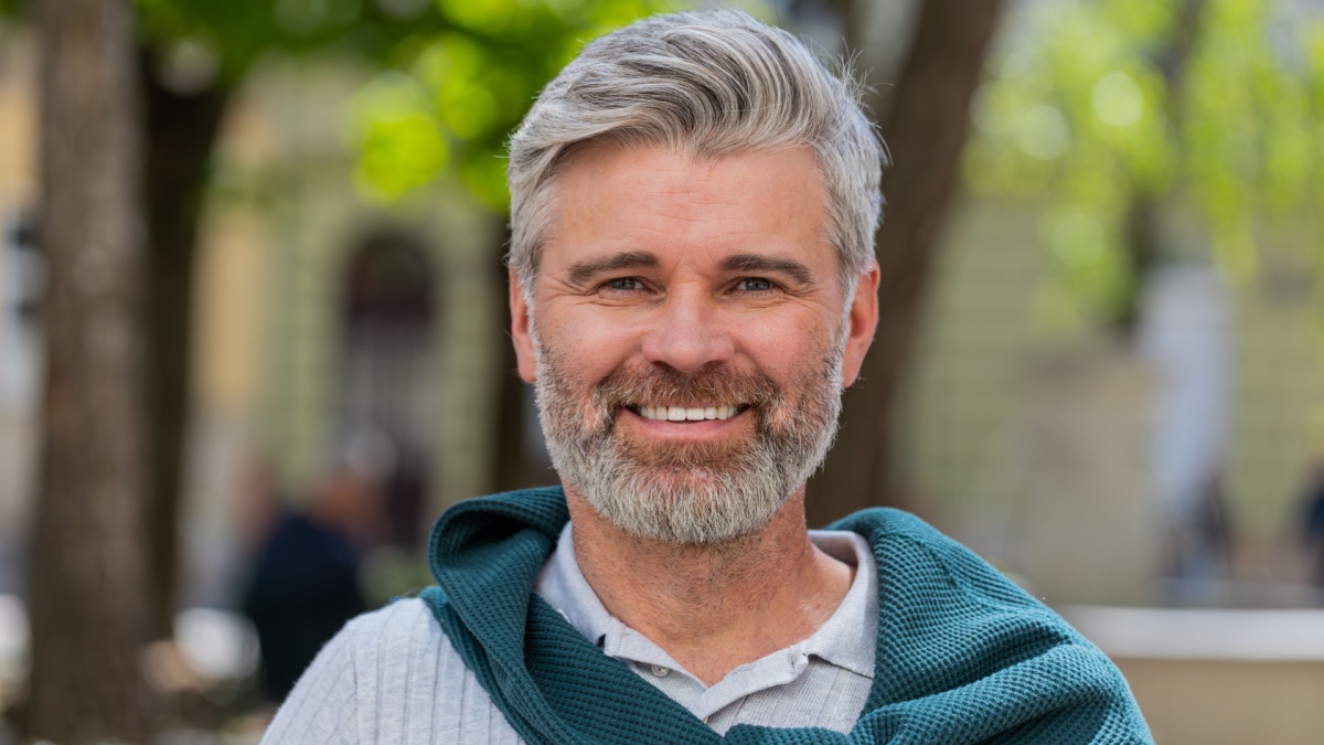 Portrait of happy bearded middle-aged man smiling friendly glad expression looking at camera dreaming resting relaxation feel satisfied good news outdoors. Guy in urban city sunshine street background.