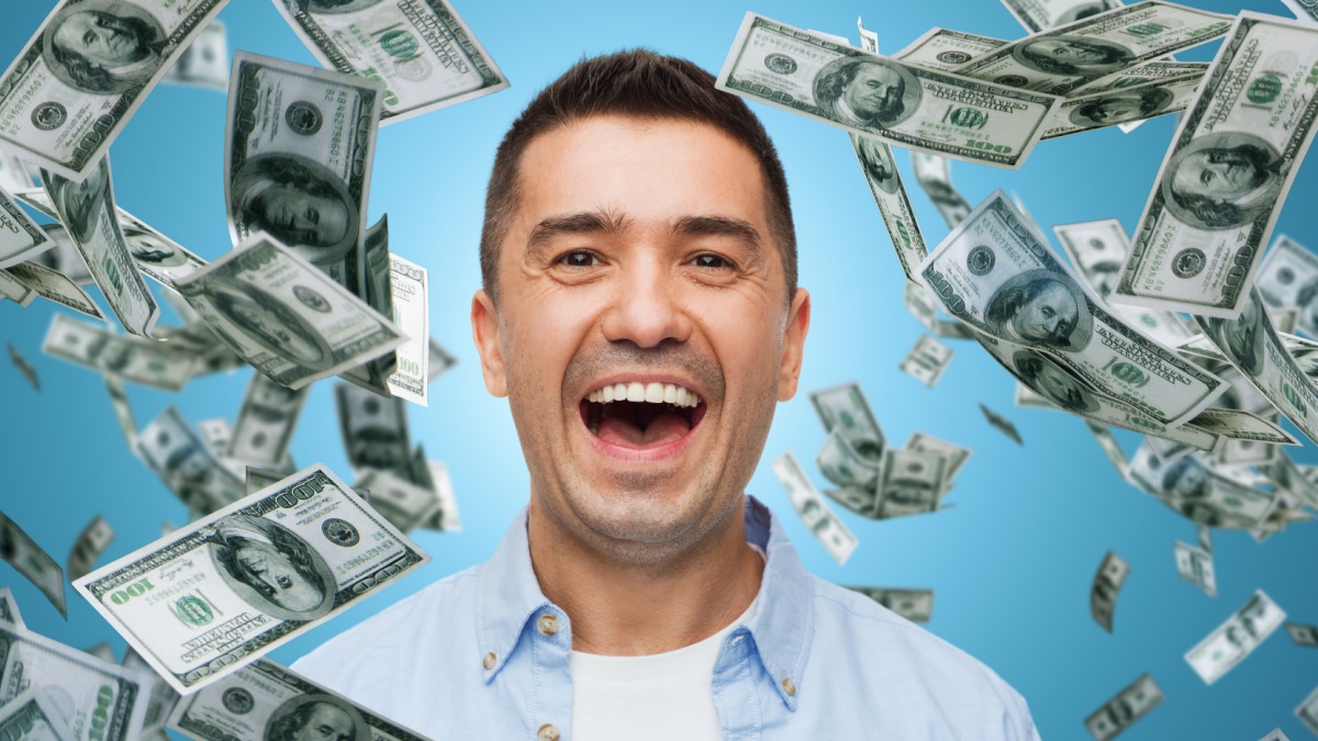 business, finance, success, emotions and people concept - laughing man over blue background with heap of falling dollar money.