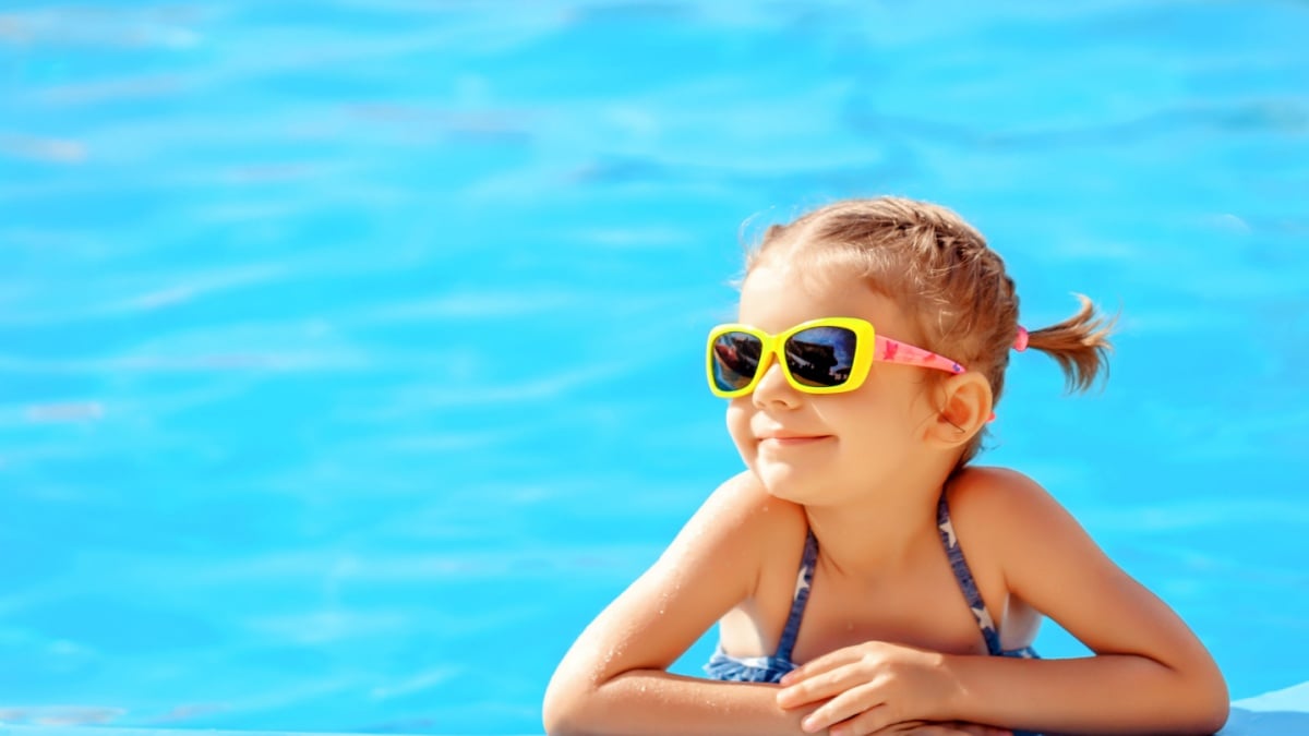 Smiling cute little girl in sunglasses in pool in sunny day.