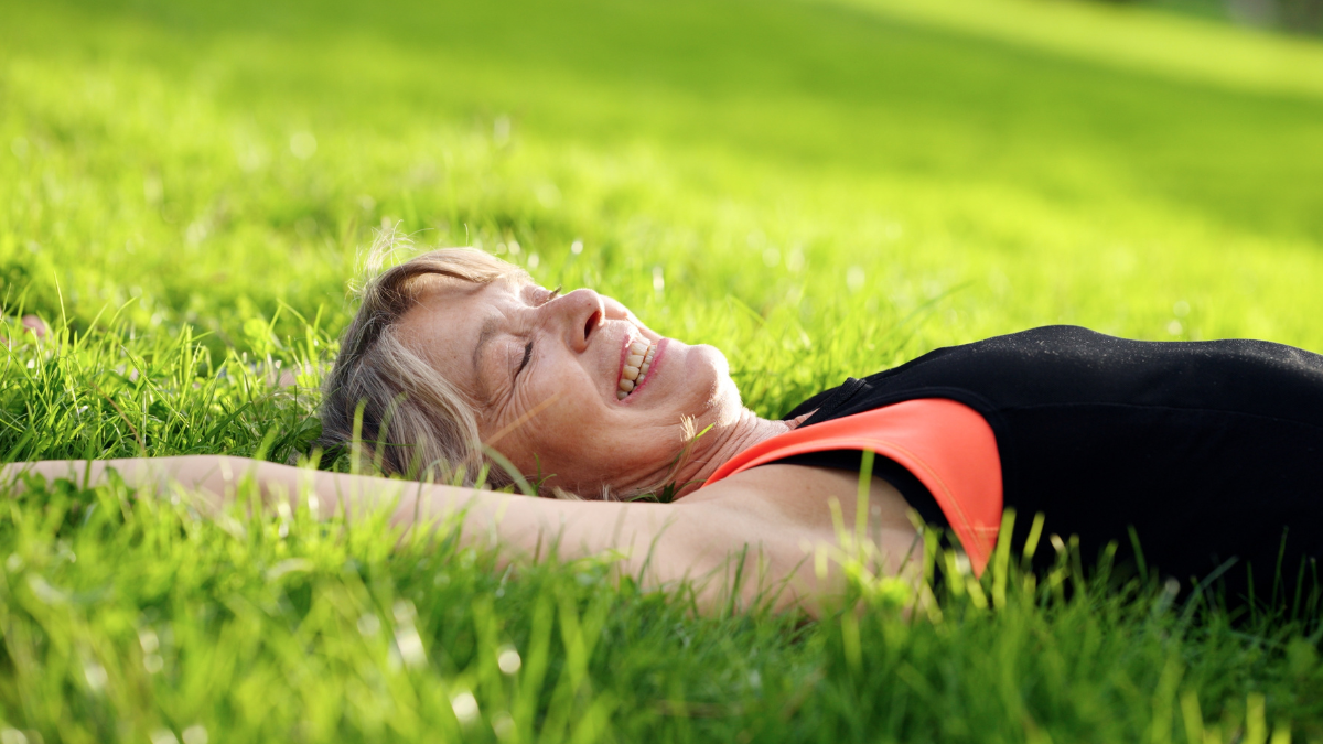 Happy senior woman resting in green grass with eyes closed, enjoying a peaceful moment outdoors and a healthy lifestyle genius life hacks.