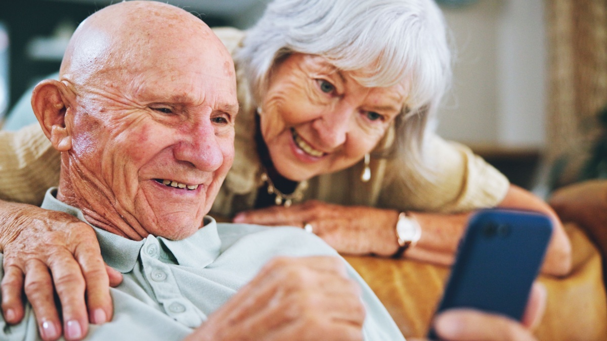 Senior couple, phone and reading on couch with hug, choice and click with video, download or search in home.