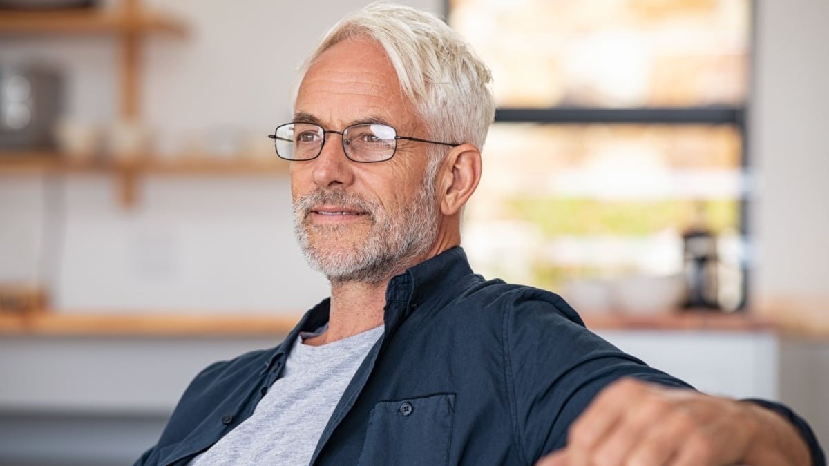 Retired mature man sitting on couch wearing spectacles and thinking. Smiling old man planning the retirement.