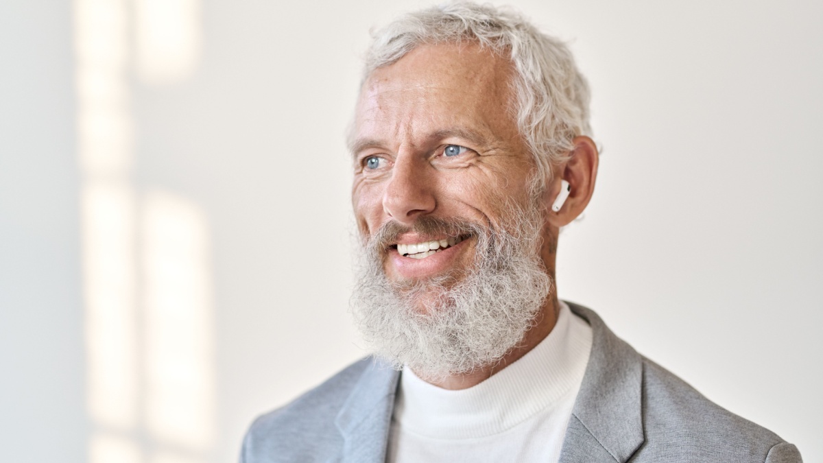 Thoughtful smiling bearded old senior business man wearing earbud.