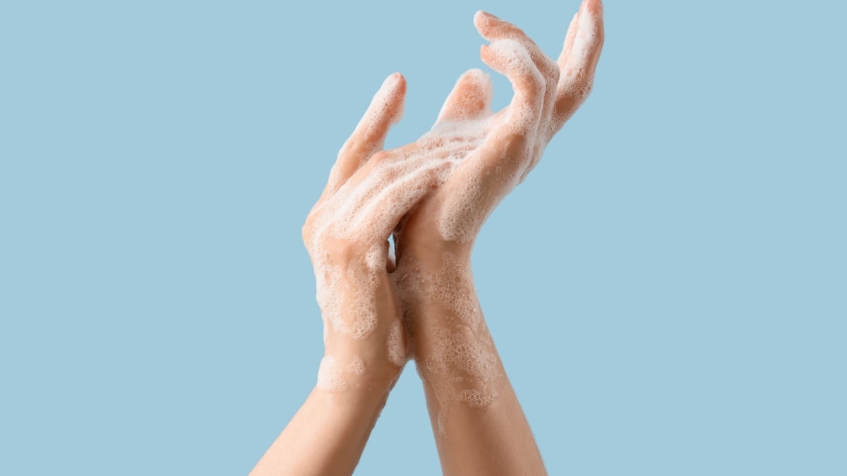 Hands in soap foam on light blue background.