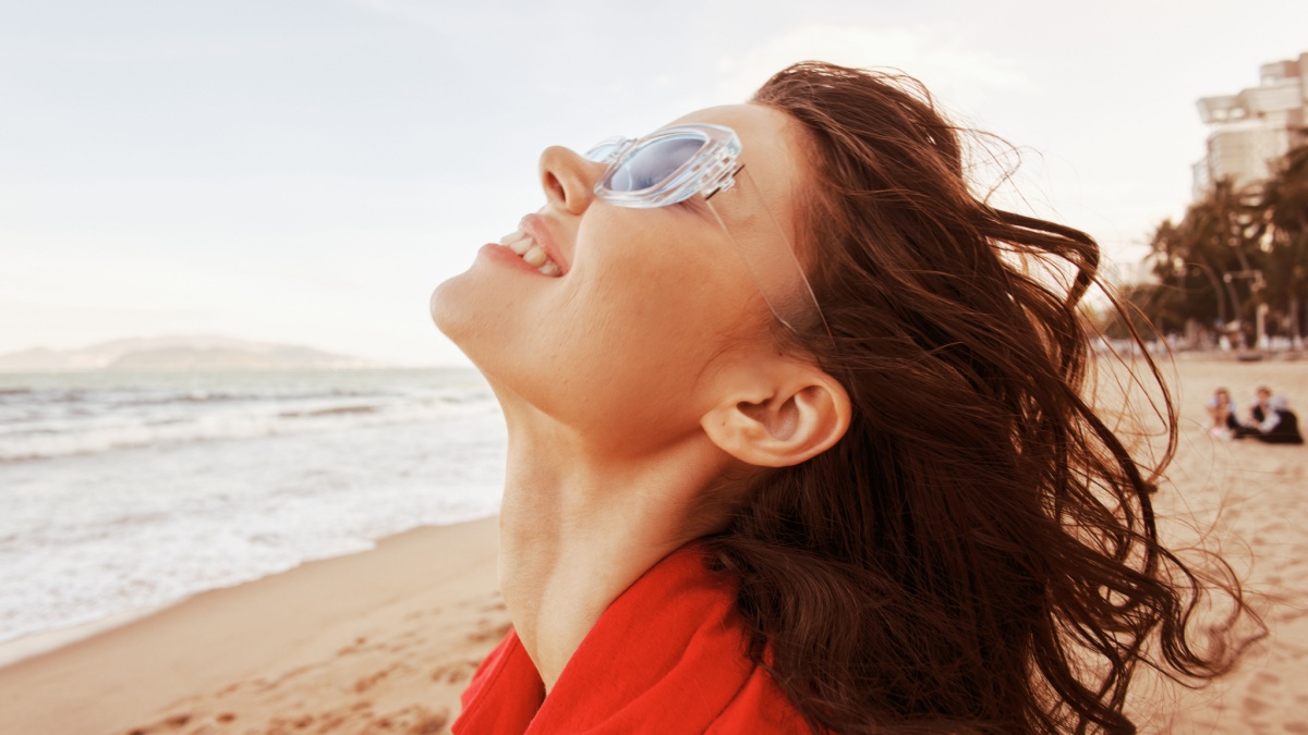 Smiling Woman at the Beach, Enjoying the Sea Breeze and Sunset Embracing Freedom and Happiness in Trendy Sunglasses.