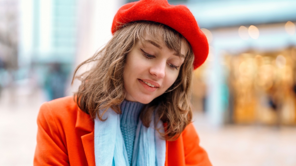 closeup of portrait of young woman in red coat and beret having coffee at the side cafe outside.