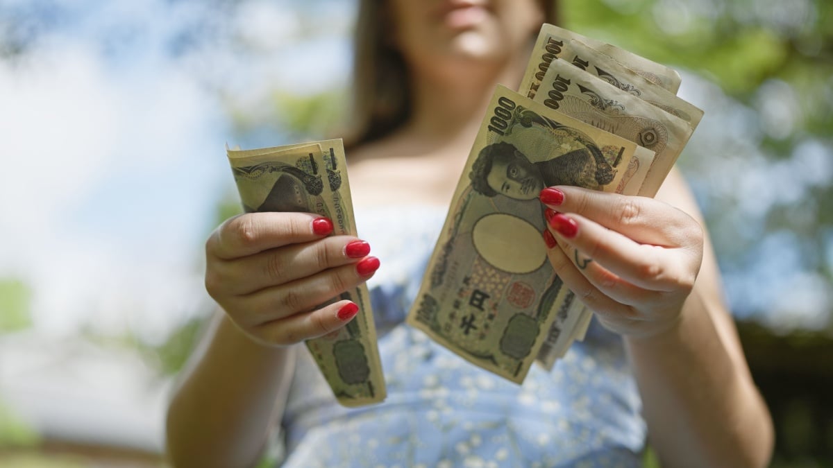 Thrifty young woman counting heap of yen banknotes amidst the lush green of a traditional japanese park, cementing her financial freedom.
