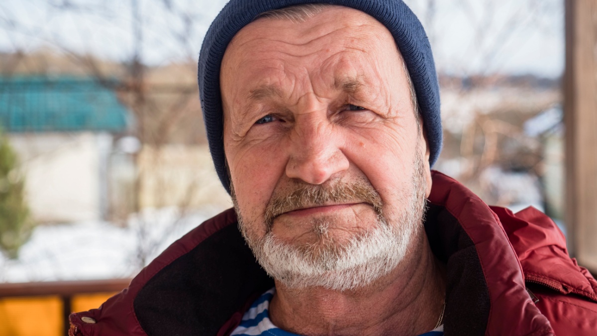 Elderly village man outdoors in winter in warm clothes.