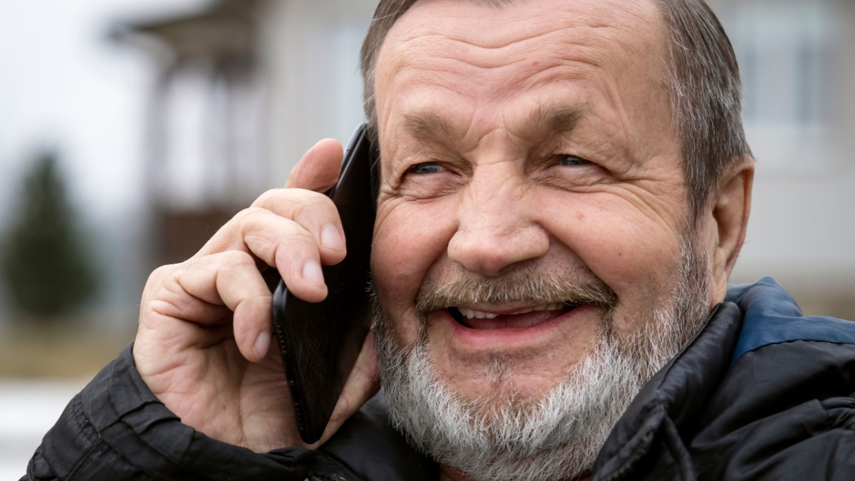 Happy elderly man uses a smartphone in warm clothes in winter, close-up portrait.