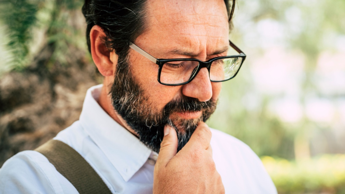 Worried adult caucasian 50 years old man touch the beard and think alone.