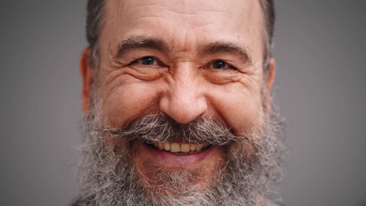 Portrait of positive bearded elderly man smiling isolated on gray background.