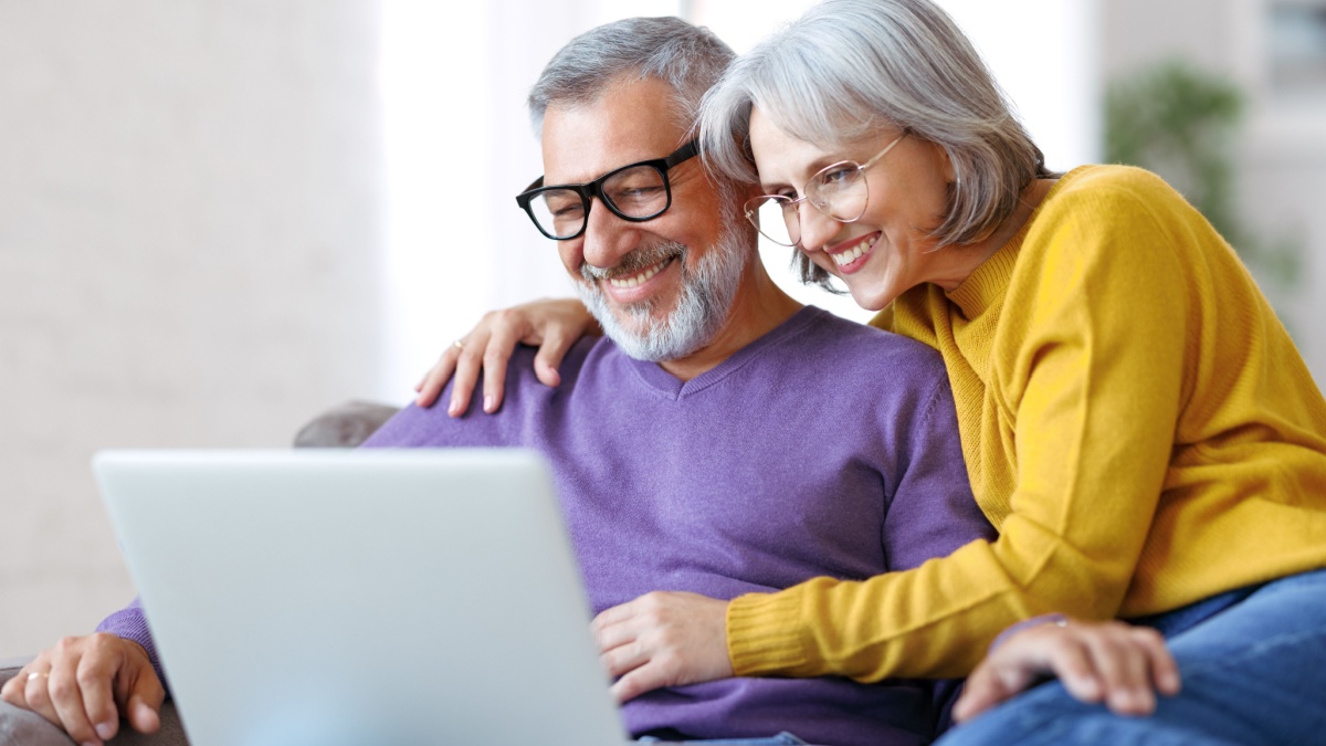 Beautiful mature family couple looking at laptop with smile on face while spending great time together at home on retirement.
