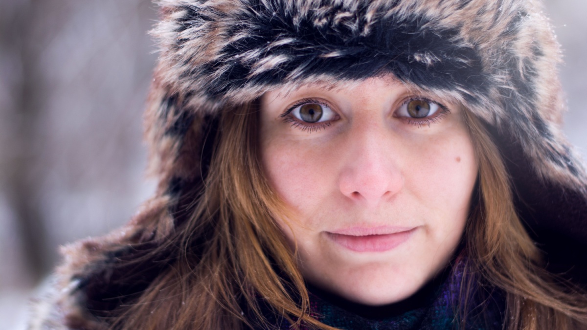 Young caucasian woman in winter hat and coat. Headshot photo in snowy forest in winter.