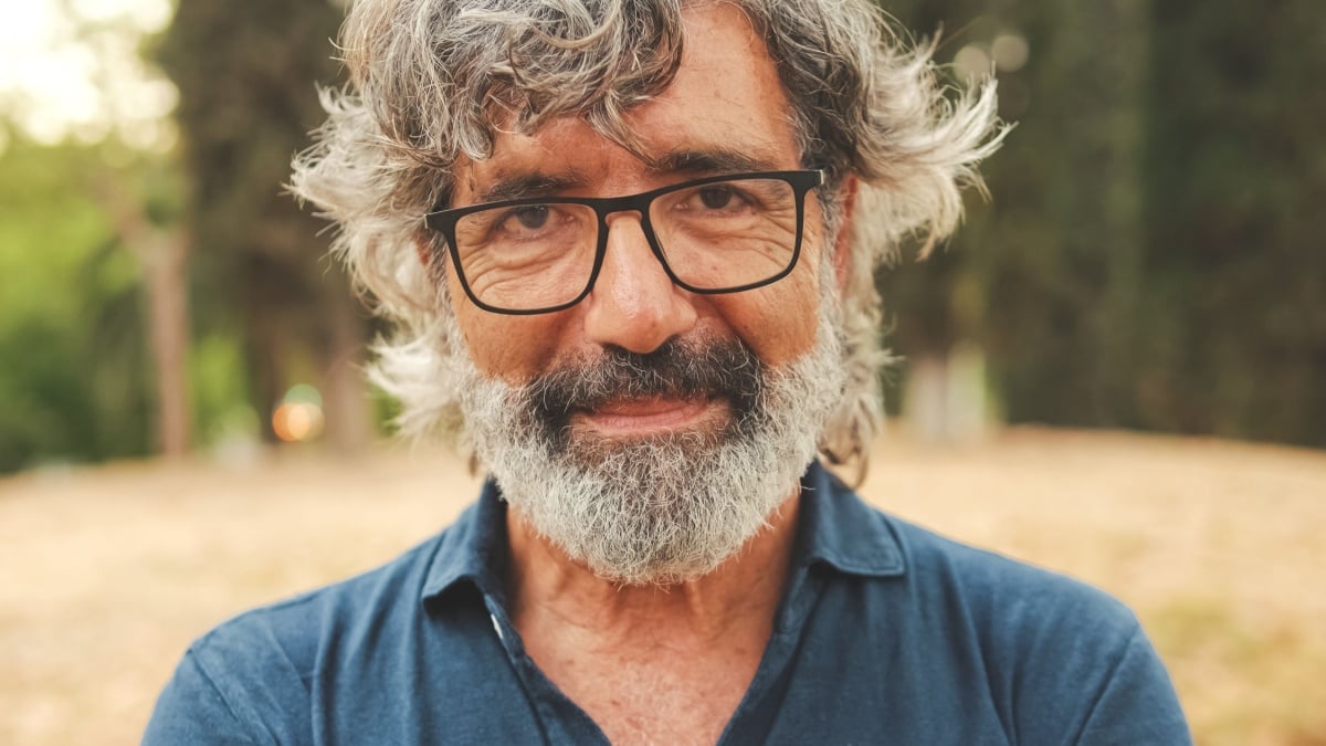 Close-up of retired man with glasses crossing his arms and looking at the camera with smile while standing in the park.