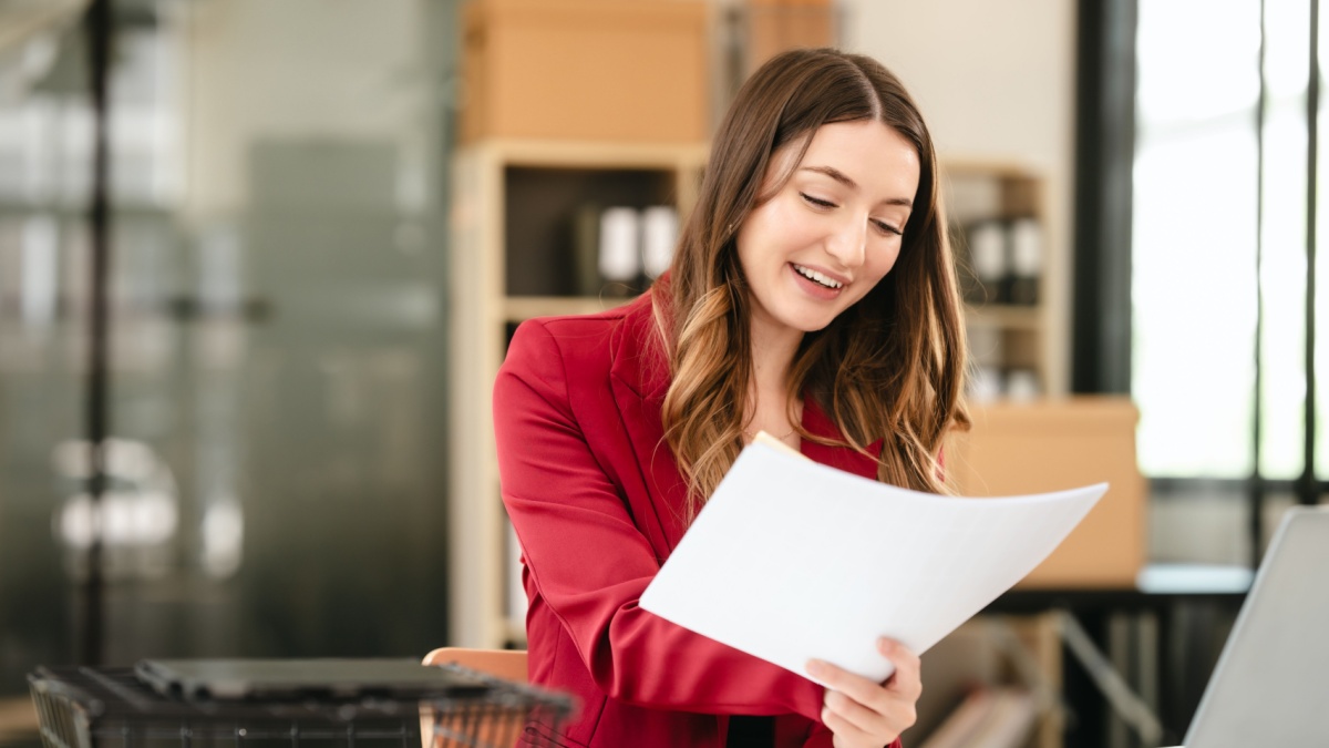 Caucasian businesswoman, likely an accountant or CPA, smiling and holding a coffee cup while working on her laptop.