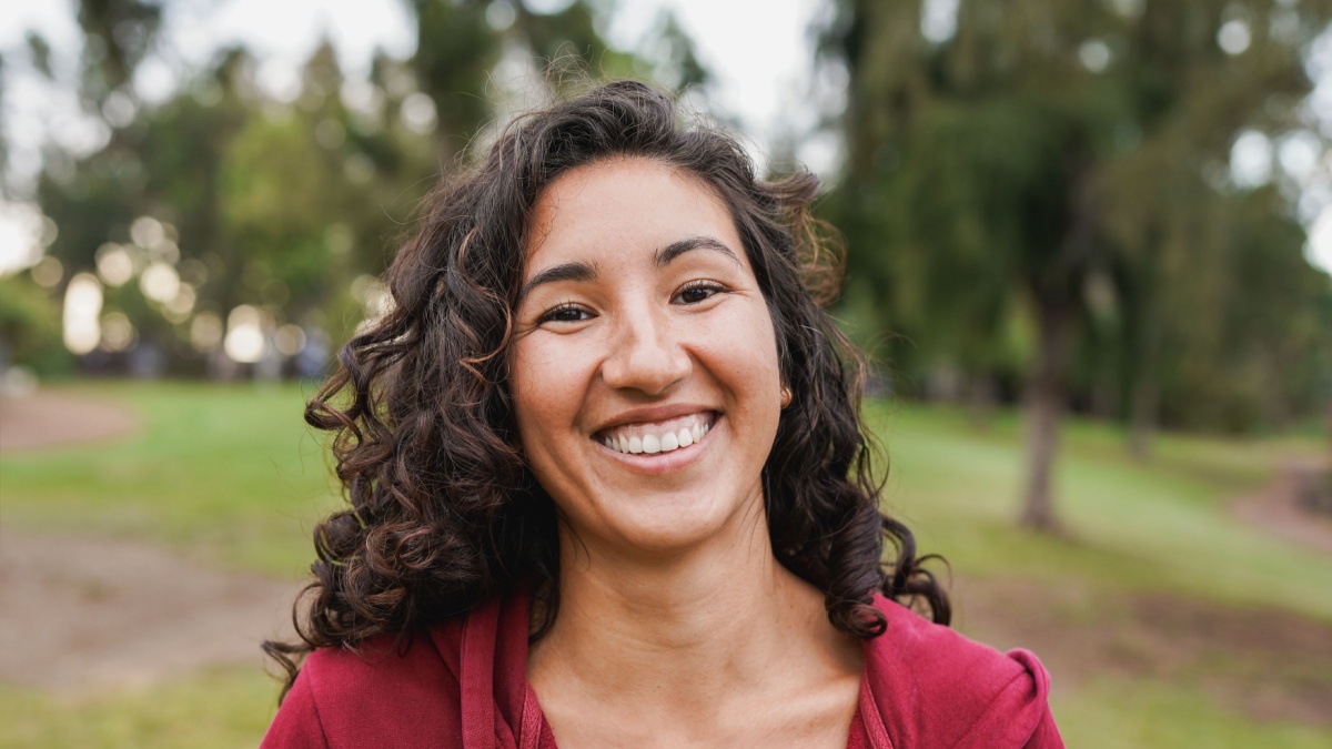 Portrait of native american woman smiling on camera with city park in background - Indigenous girl outdoor.