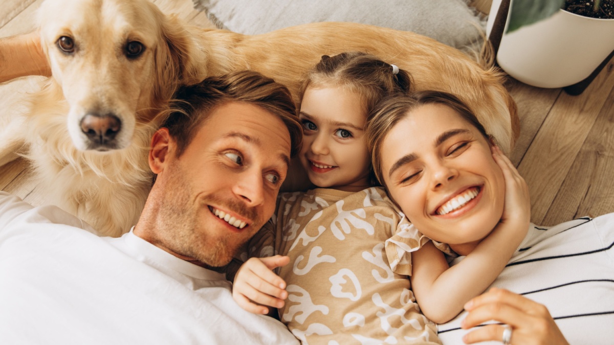 Smiling, beautiful family and golden retriever hugging together, lying, embracing in cozy living room at home.