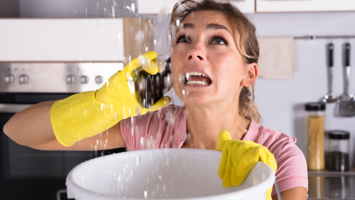 Shocked Woman Calling Plumber While Collecting Water Leaking From Ceiling Using Utensil.