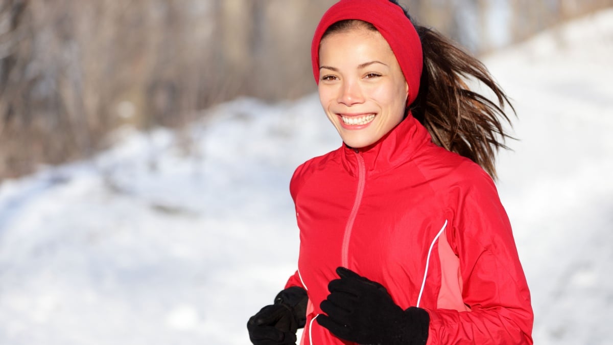 Fitness running woman in winter. Runner closeup of happy active sport model jogging in snow in winter forest. Beautiful mixed race asian chinese caucasian female model.