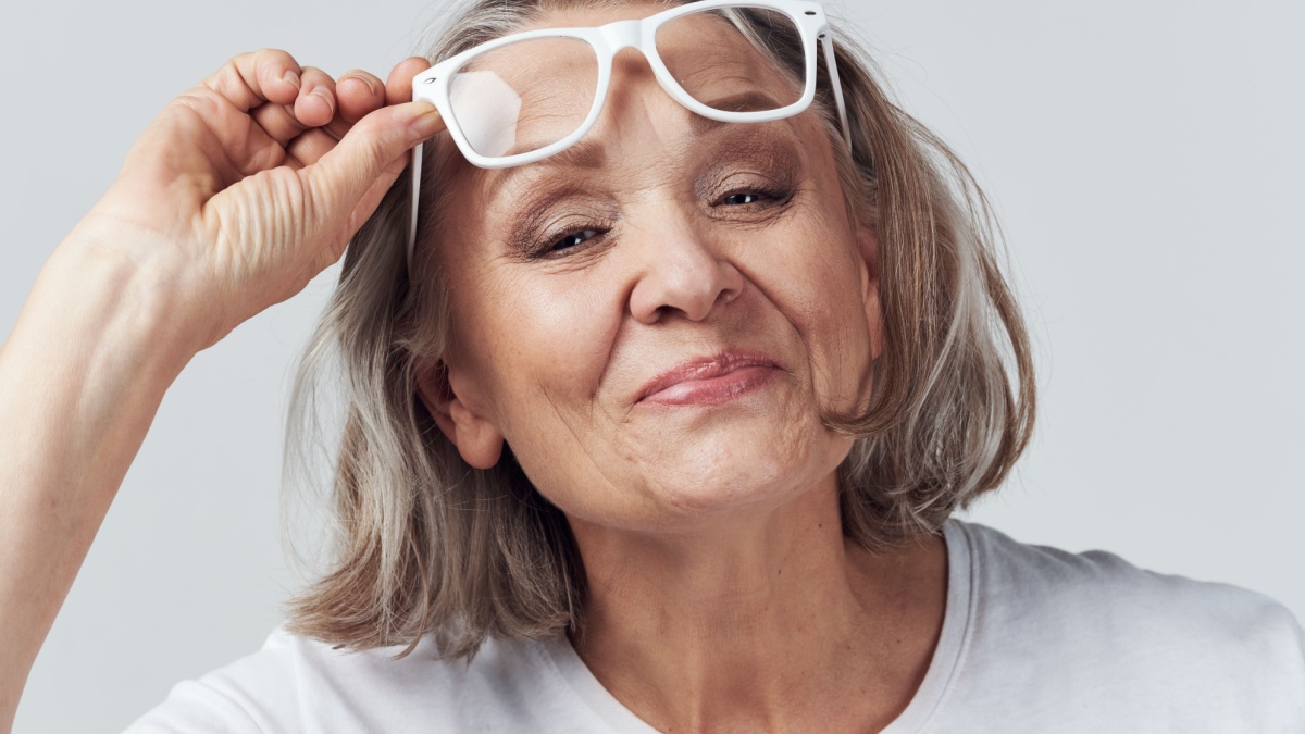 Beautiful elderly woman lifts her glasses on her forehead.