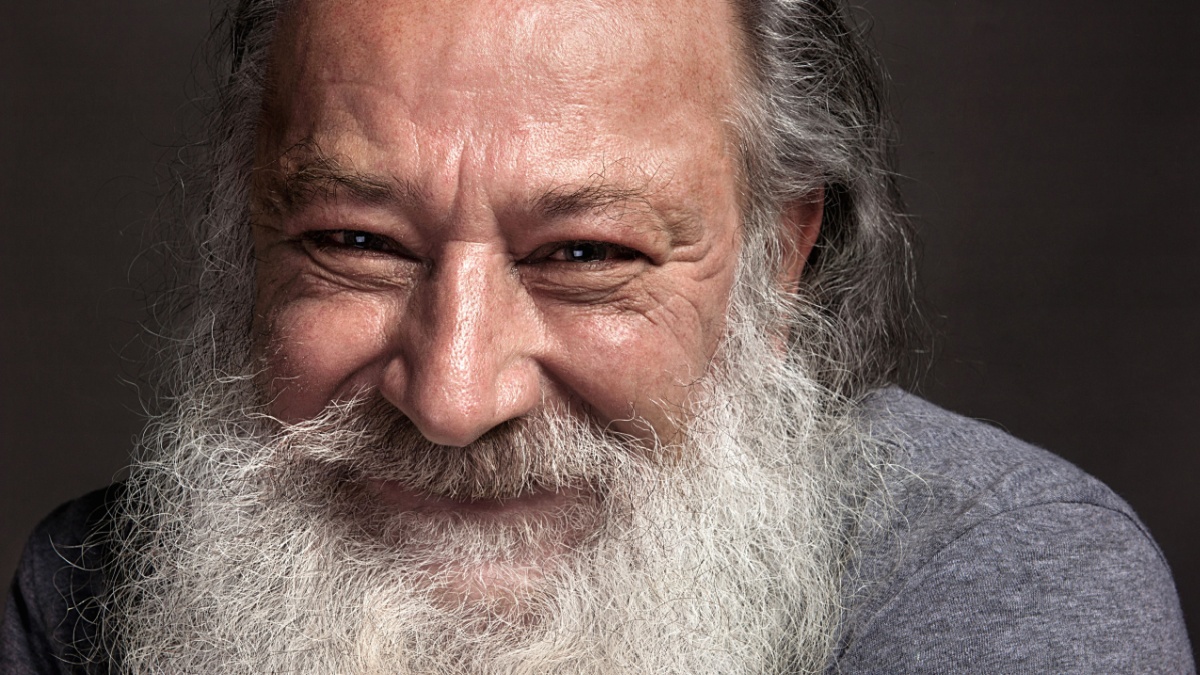 old man sixty, seventy, with a long beard with big smile on a dark background.