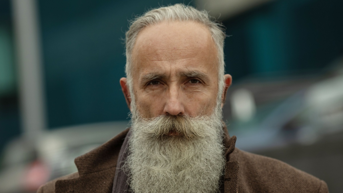 Fashionable senior man with gray hair and beard is outdoors on the street..