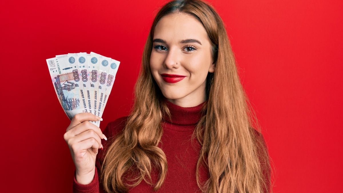 Young blonde woman holding russian 500 ruble banknotes looking positive and happy standing and smiling with a confident smile showing teeth