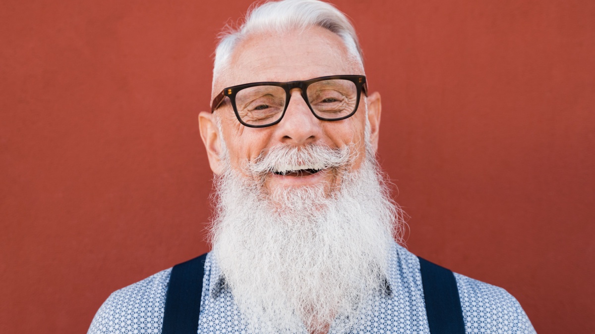 Portrait of happy hipster senior man smiling on camera with red background - Focus on face.