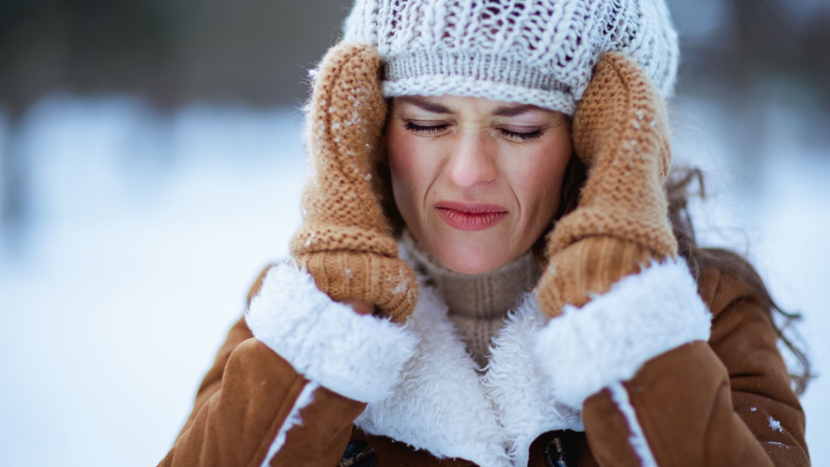 stressed modern woman with mittens in a knitted hat and sheepskin coat outside in the city park in winter.