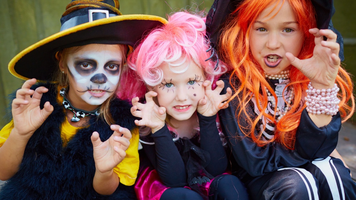 Portrait of three little girls in Halloween costumes looking at camera with frightening gesture.