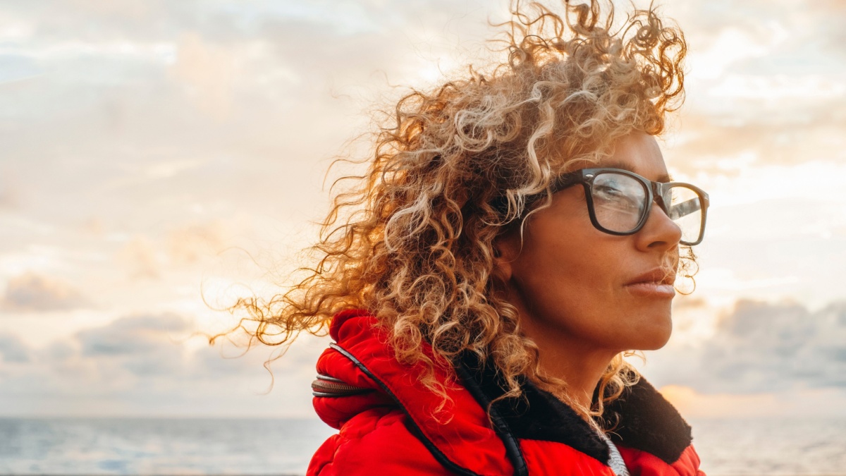 Side portrait of attractive woman in travel outside activity with curly hair moved by the wind. Concept of independence. Female people enjoy journey trip adventure lifestyle. Wearing eyewear. Freedom.