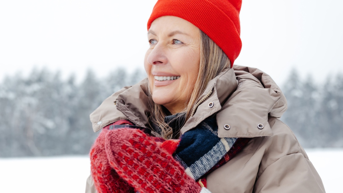 Smiling mature woman in red hat having hot tea outdoors.