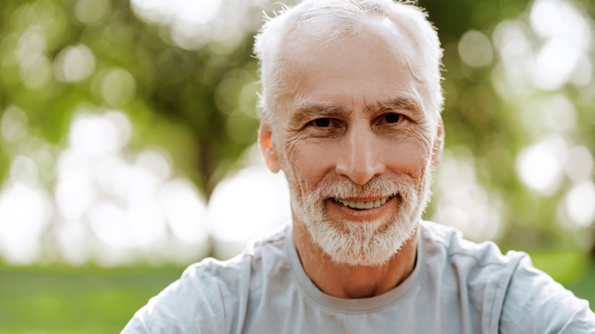 Portrait of happy senior gray haired man smiling while enjoying sunny day at park.