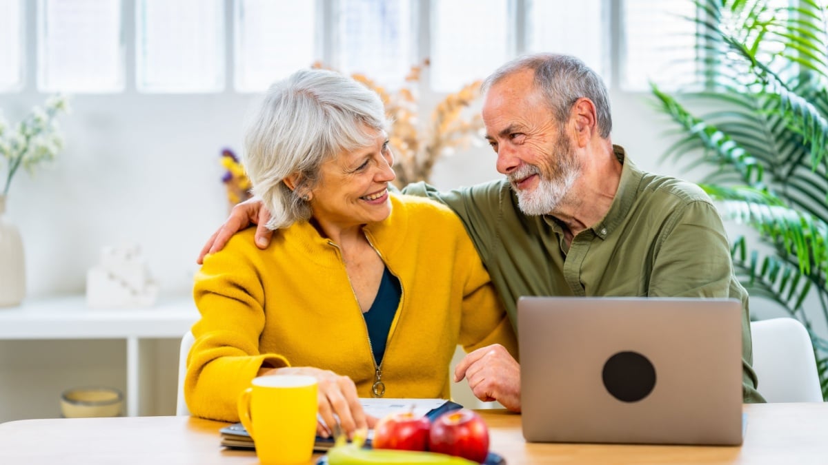 Senior couple celebrating good news on household budget sitting on the living room using laptop.