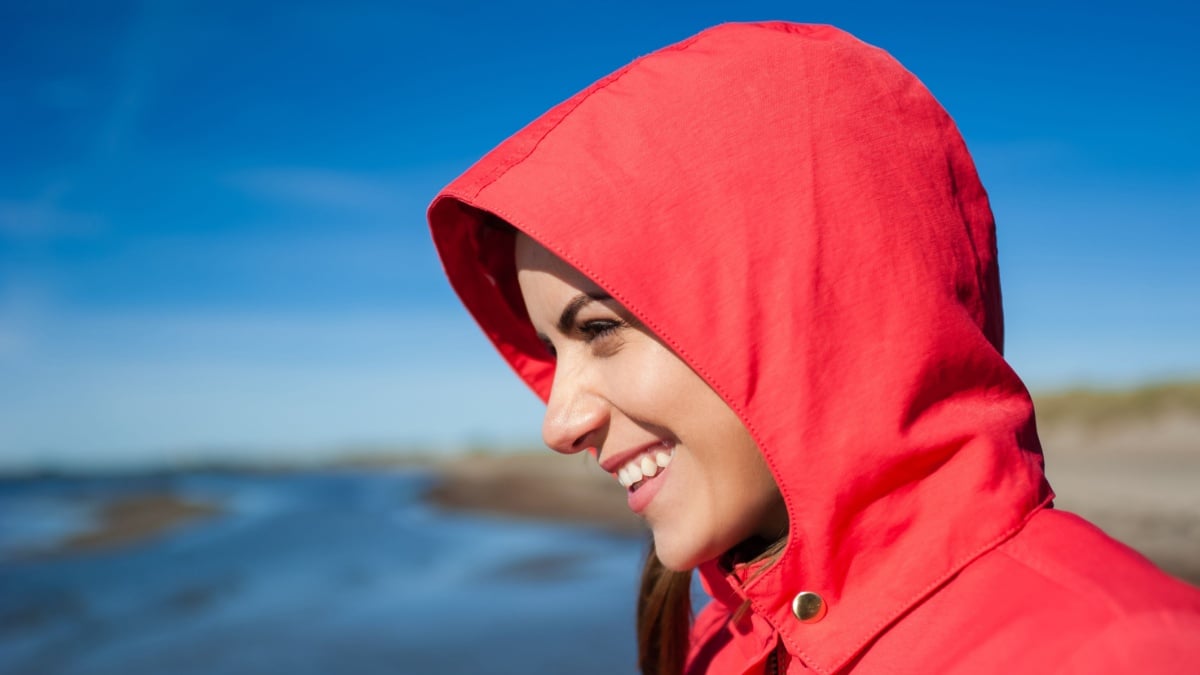 Young woman near sea, smiling, with a red jacket.