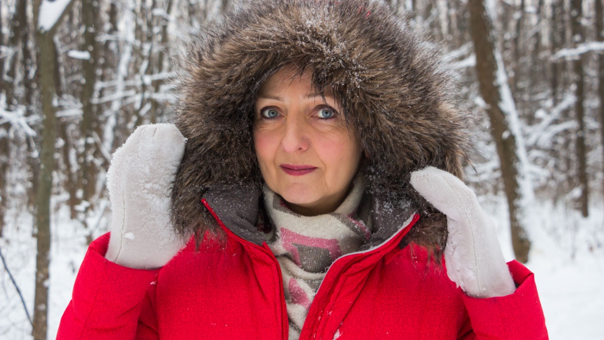 Portrait of a nice senior woman in the winter snow wood in red coat.
