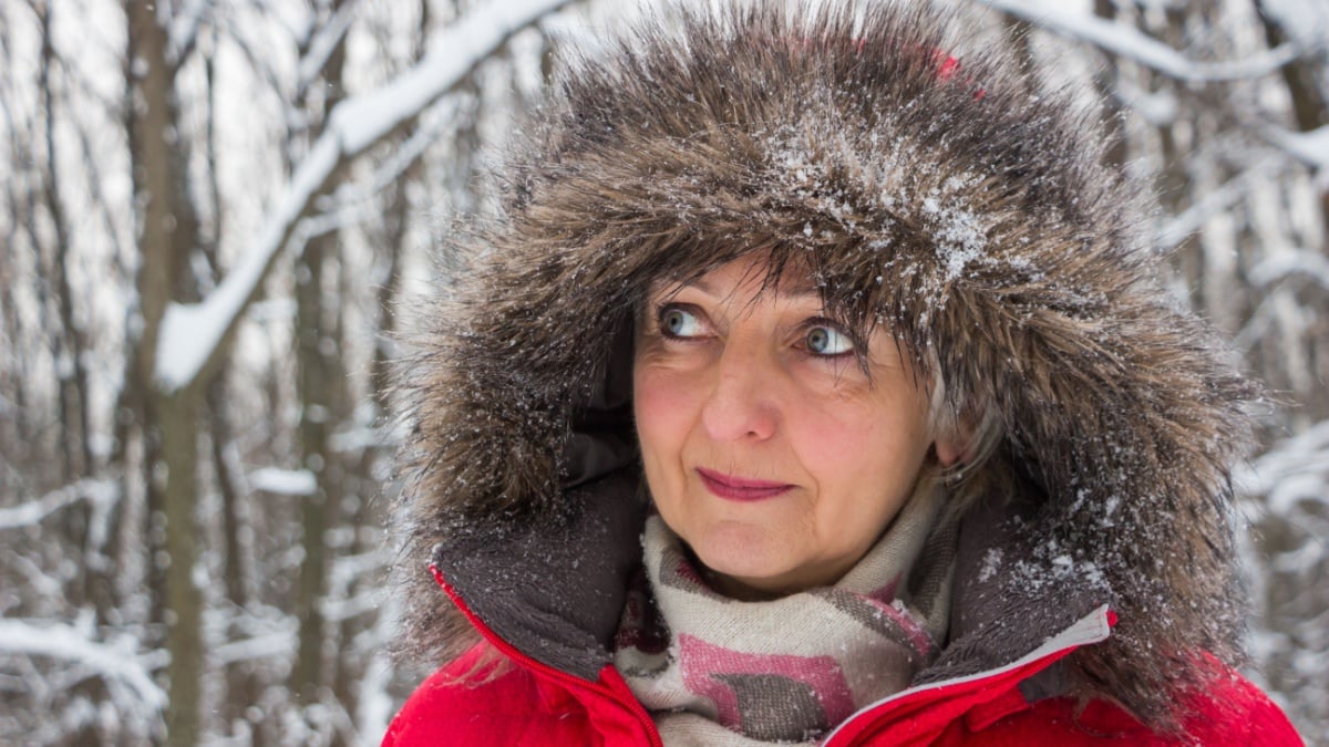 Portrait of a nice senior woman in the winter snow wood in red coat.