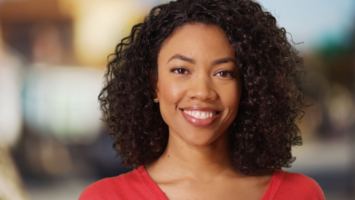 Smiling young African woman looking cheerfully at camera on blurred background.