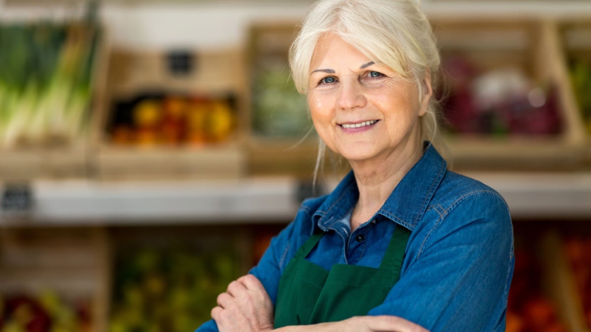 Portrait of confident owner with arms crossed standing in small grocery store.