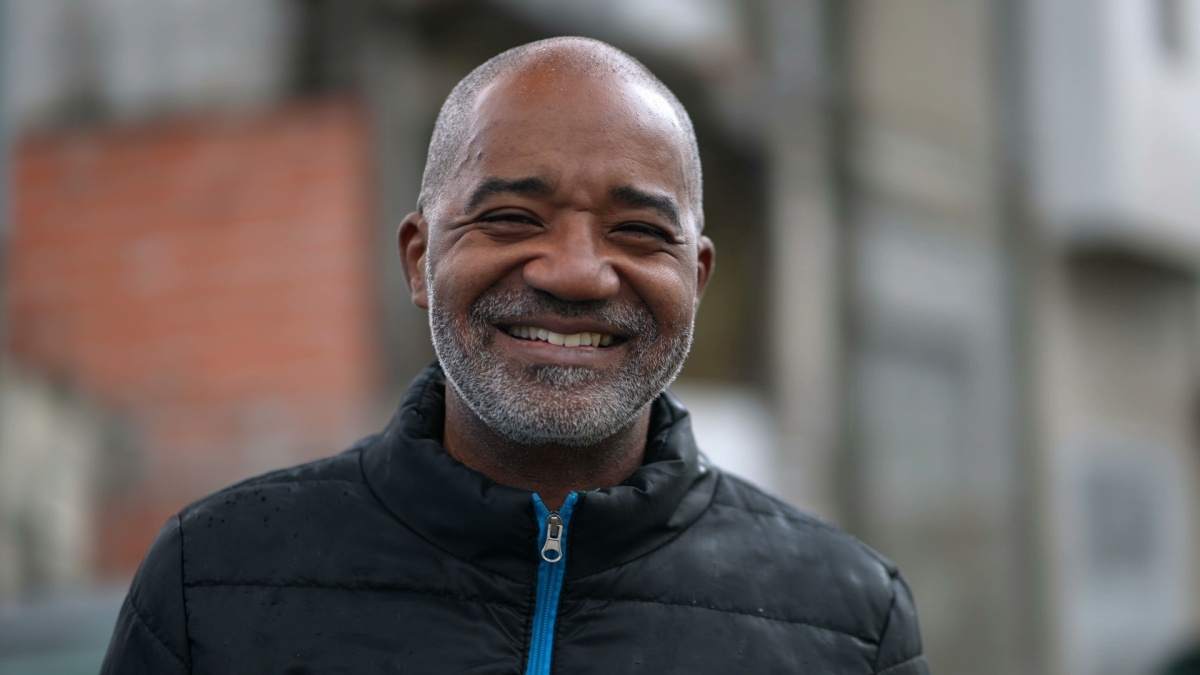 A happy senior black man portrait face smiling at camera standing outside in street.