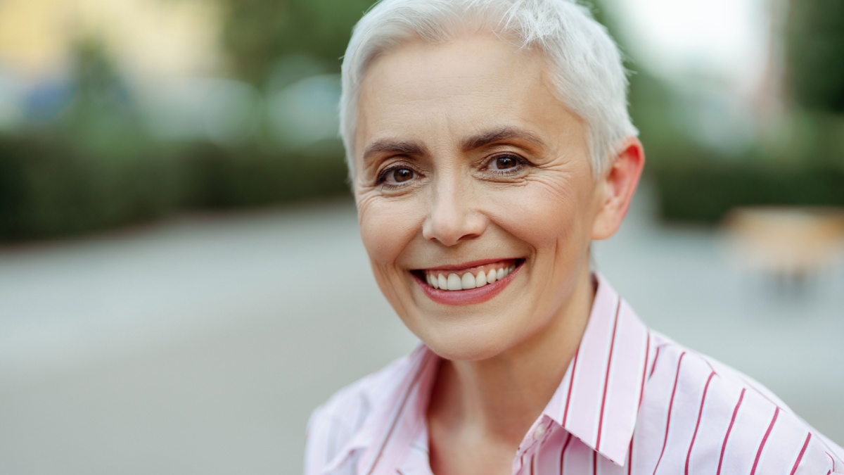 Portrait of smiling senior woman looking at camera on the street with blurred background. Successful business concept.