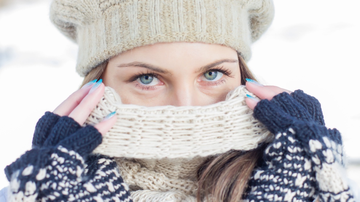 Winter Portrait of Female with Beautiful Blue Eyes outdoor. Closeup of Young woman wearing clothing for cold weather a scarf hat and gloves.